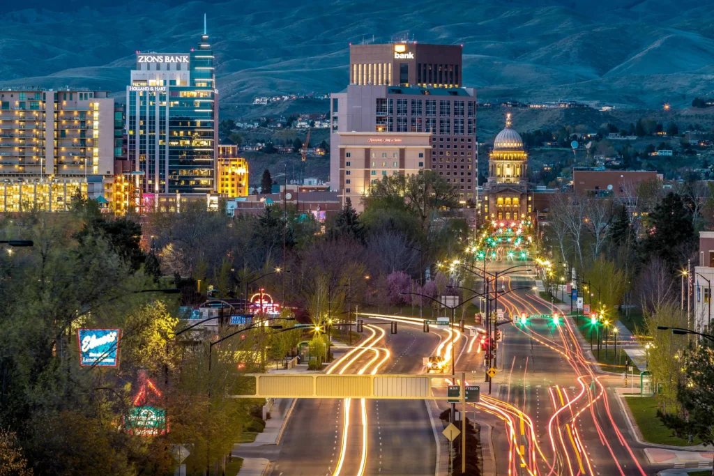 Boise cityscape at night with illuminated buildings, including the Idaho State Capitol, and streaks of car lights creating dynamic trails