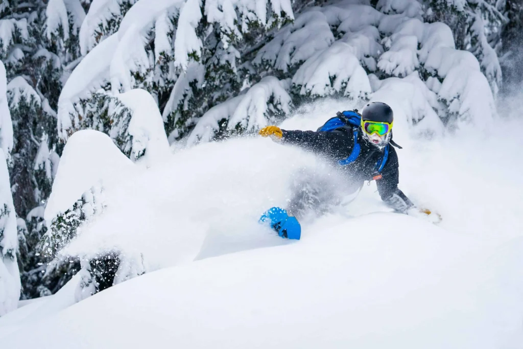 A snowboarder carving through fresh powder in a snowy forest, with trees heavily covered in white snow near Mount Bachelor, Oregon.