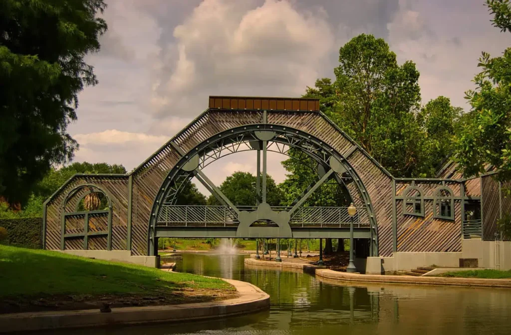 A beautifully designed arched bridge over a serene canal in Louis Armstrong Park, surrounded by lush greenery and peaceful reflections in the water