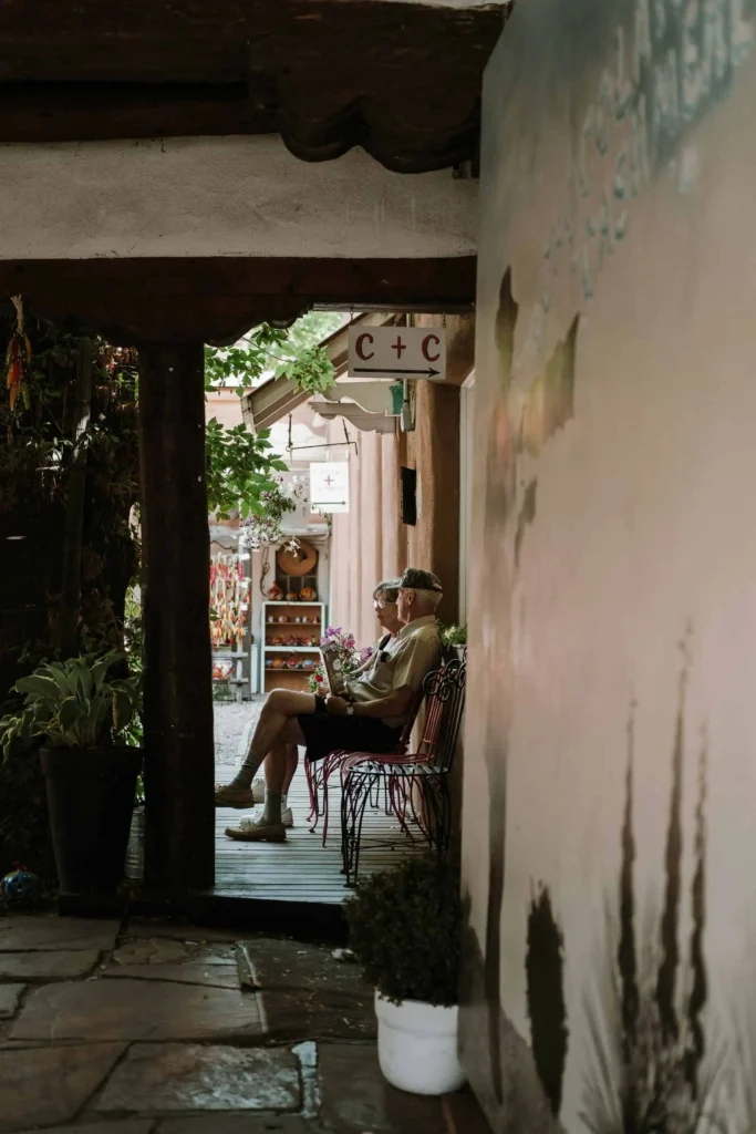 An elderly couple enjoys a peaceful moment on a bench in a charming Santa Fe alley adorned with local crafts and greenery