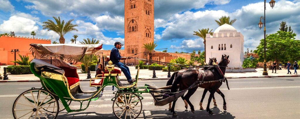 Horse-drawn carriage passing in front of the iconic Koutoubia Mosque in Marrakech, Morocco, with vibrant palm trees and a blue sky in the background