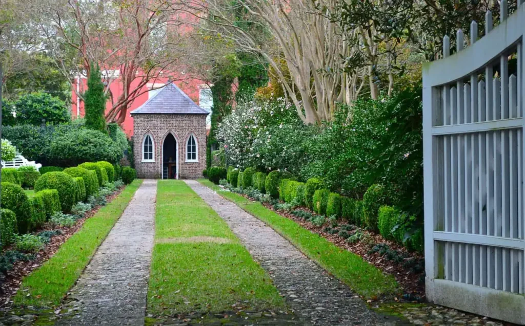 A picturesque pathway leading to a charming chapel surrounded by lush greenery and trimmed hedges, exuding tranquility and historical charm.