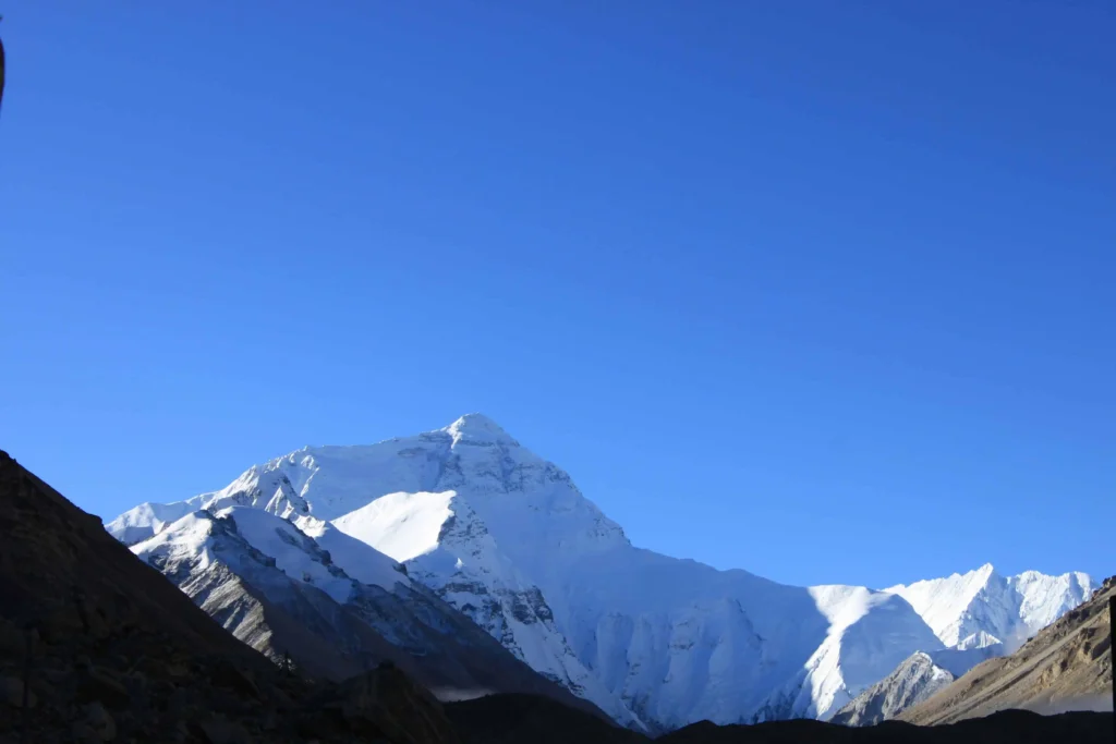 A breathtaking view of a snow-covered Mount Everest during sunrise, with hues of orange and pink lighting up the peak.