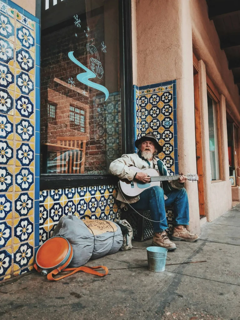 A street musician plays the guitar in front of a beautifully tiled wall in downtown Santa Fe, showcasing the city's vibrant artistic culture