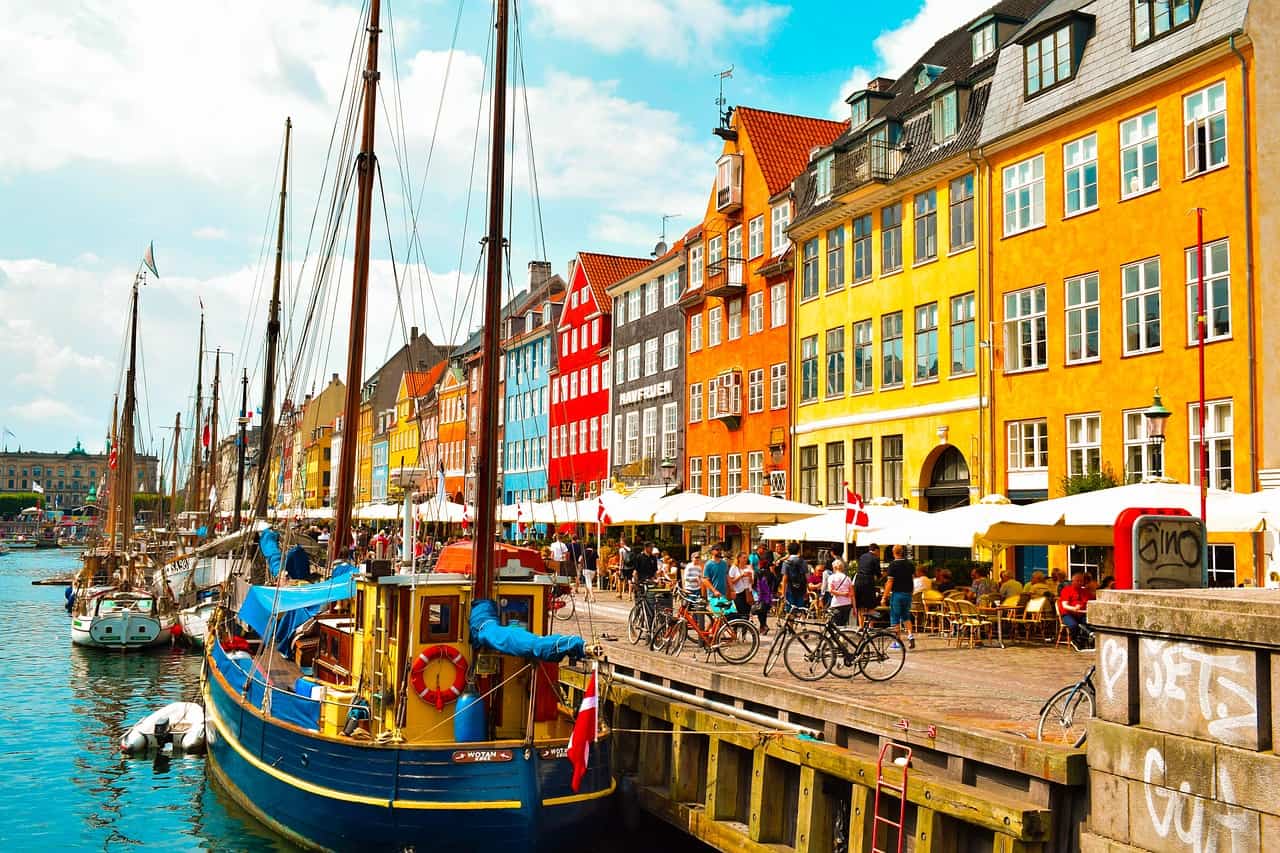 Colorful waterfront buildings and sailboats at Nyhavn Canal in Copenhagen, Denmark, with vibrant cafes and people enjoying the scenic view along the historic quay.