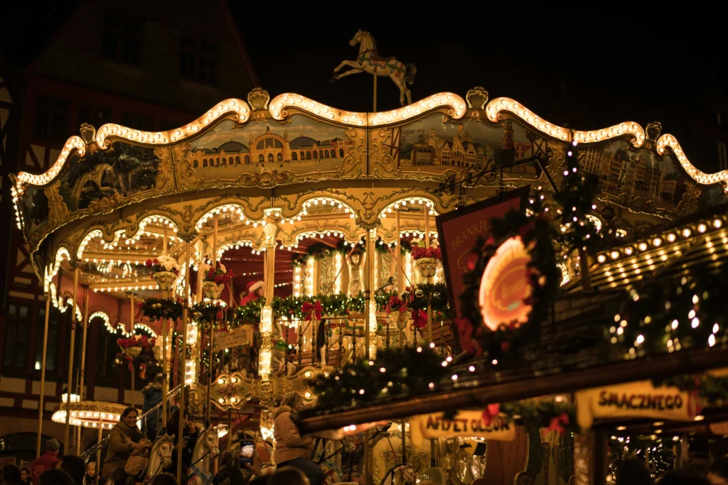 A classic carousel illuminated by golden lights at a Christmas market, with families enjoying the festive ride at night.

