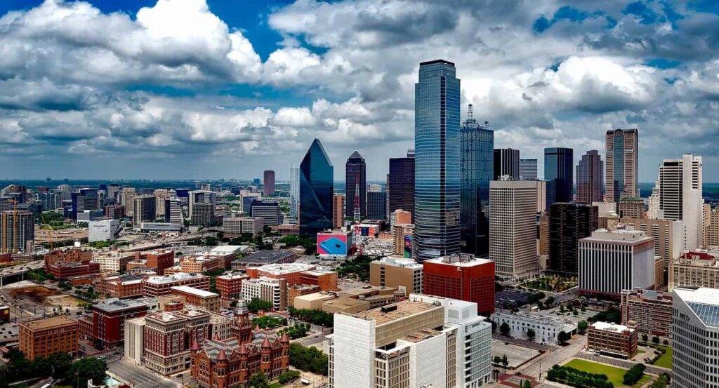 Stunning aerial view of downtown Dallas, Texas, featuring a vibrant skyline with modern skyscrapers under a partly cloudy blue sky.