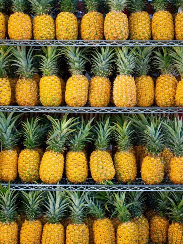 Rows of fresh, ripe pineapples stacked neatly on display, showcasing the vibrant tropical fruit commonly found in Kona, Big Island, Hawaii.