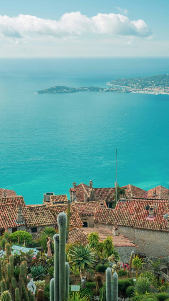 A scenic overlook of Eze France featuring the village's terracotta rooftops against the deep blue waters of the Mediterranean, with boats gently sailing in the distance