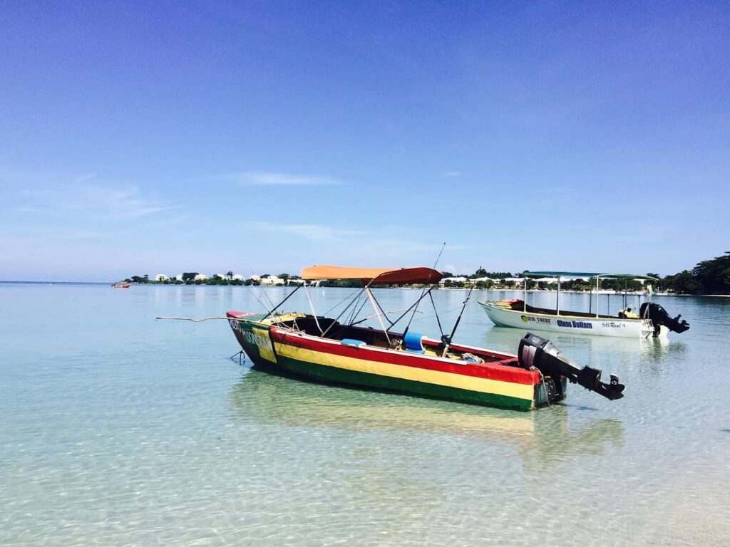 Two colorful fishing boats floating on the calm, crystal-clear waters of Negril, Jamaica, against a backdrop of a bright blue sky.