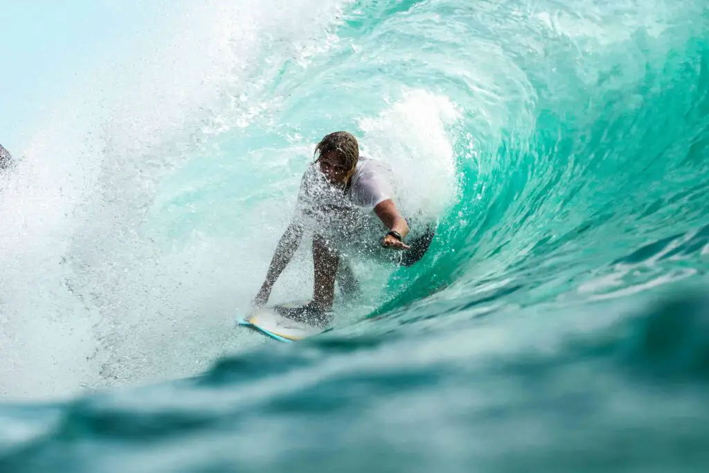 A surfer riding inside a powerful turquoise wave, perfectly positioned within the barrel as ocean spray surrounds them.
