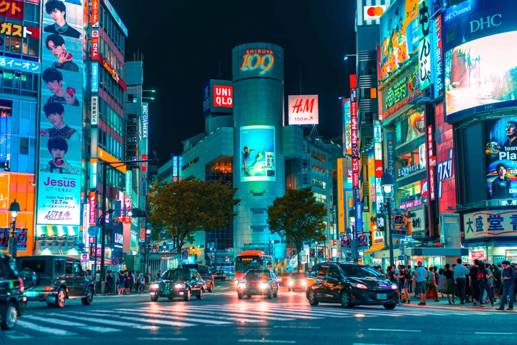 Shibuya Crossing at night in Tokyo, Japan, illuminated by vibrant neon lights, showcasing bustling streets and iconic billboards.