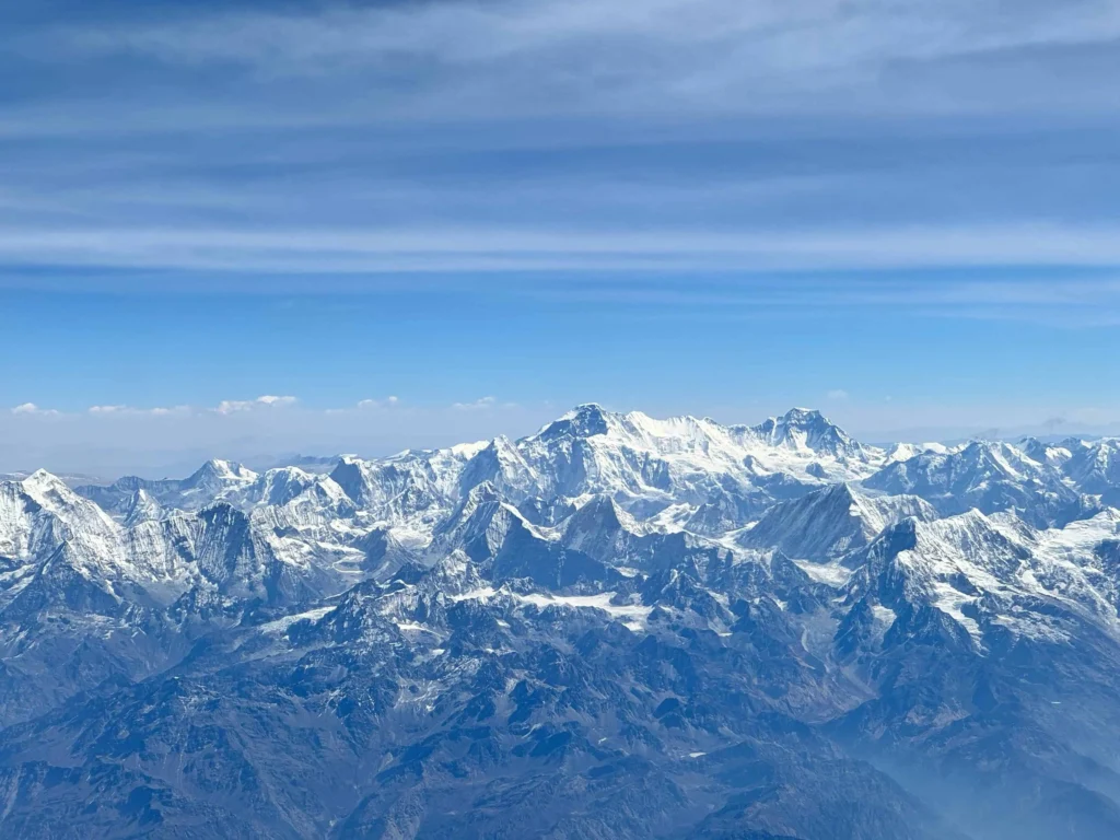 Panoramic view of the Himalayan mountain range, including Mount Everest, under a clear blue sky, showcasing its rugged beauty.