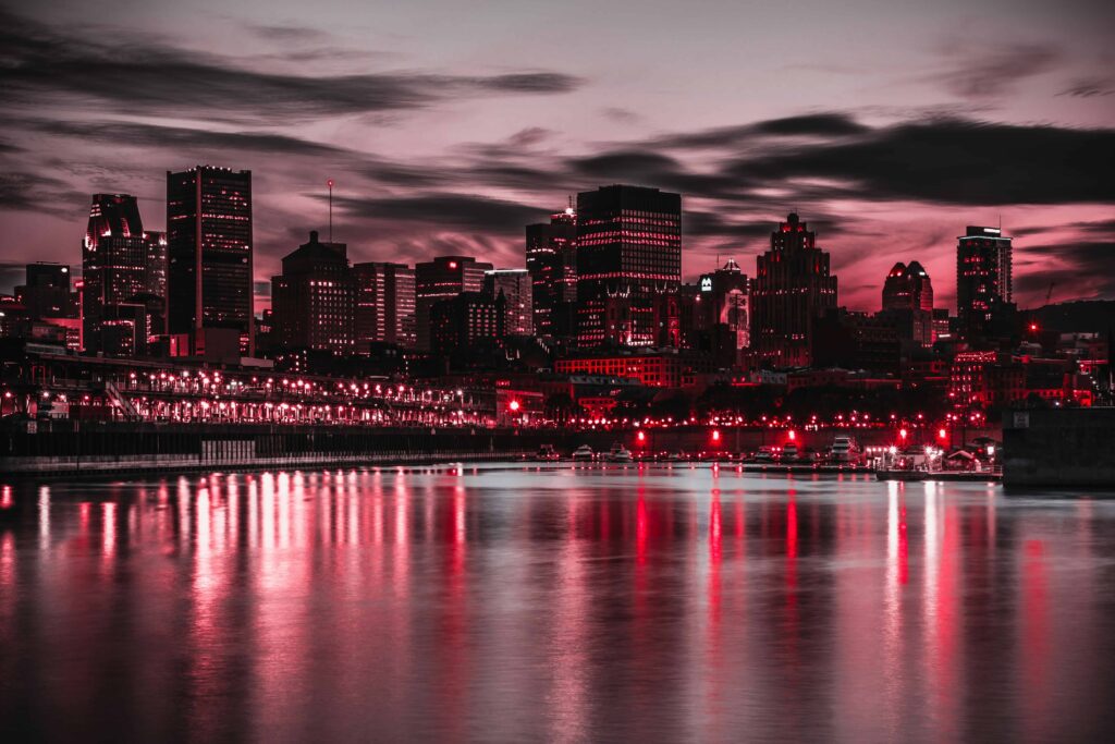 Quebec City skyline at night, reflecting red hues in the water, with a dramatic sky overhead.