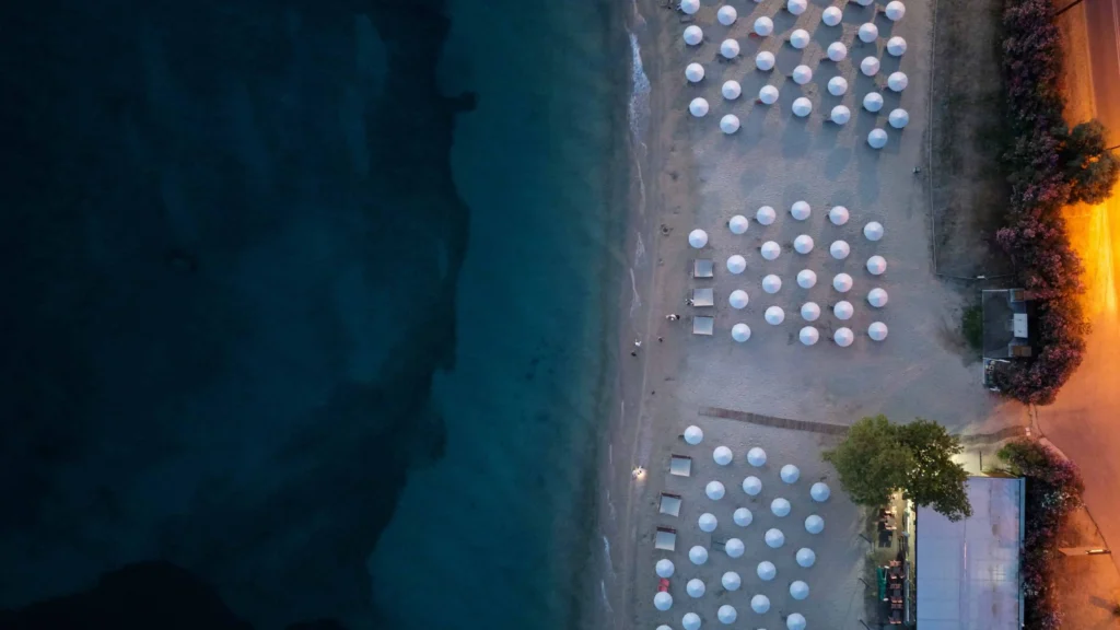 Honeymoon destinations all inclusive Greece: Aerial view of a serene Greek beach with rows of white umbrellas and clear blue waters, offering a peaceful and romantic retreat for couples.