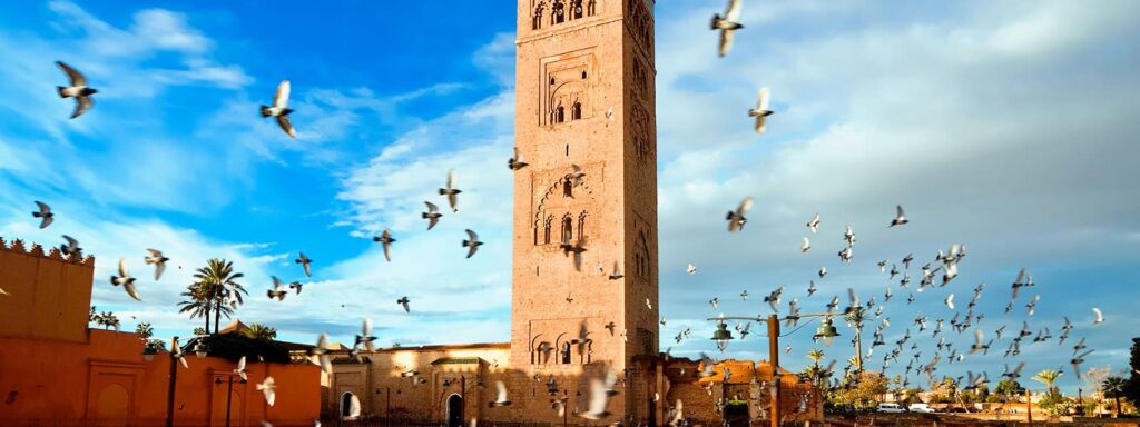 The historic Koutoubia Minaret in Marrakech surrounded by birds flying in the clear blue sky.