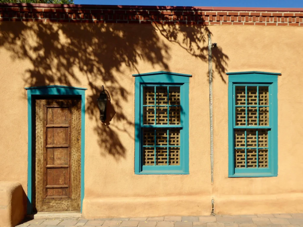 An adobe-style building with turquoise-framed windows and door, reflecting the classic architecture and cultural essence of Santa Fe.