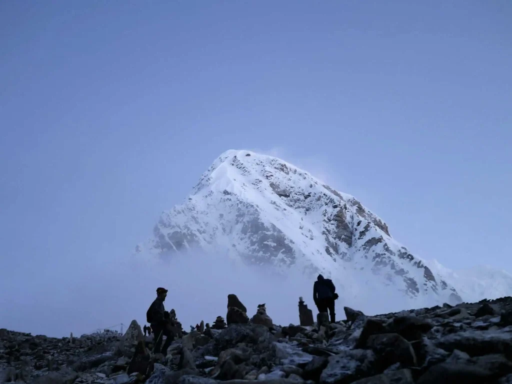 Climbers silhouetted against the backdrop of a snow-covered peak near Mount Everest, with a dramatic, mist-filled atmosphere