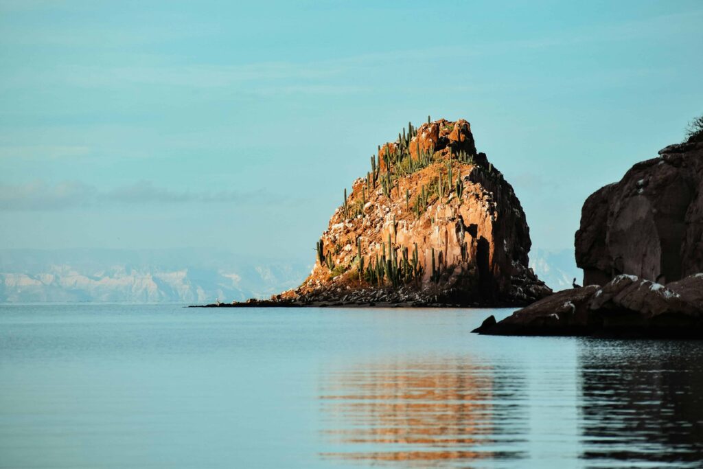 Stunning view of Isla Espíritu Santo in La Paz Mexico, with a rocky outcrop covered in cacti reflected in the calm, clear waters of the Sea of Cortez, capturing the natural beauty and serene atmosphere of this breathtaking destination.