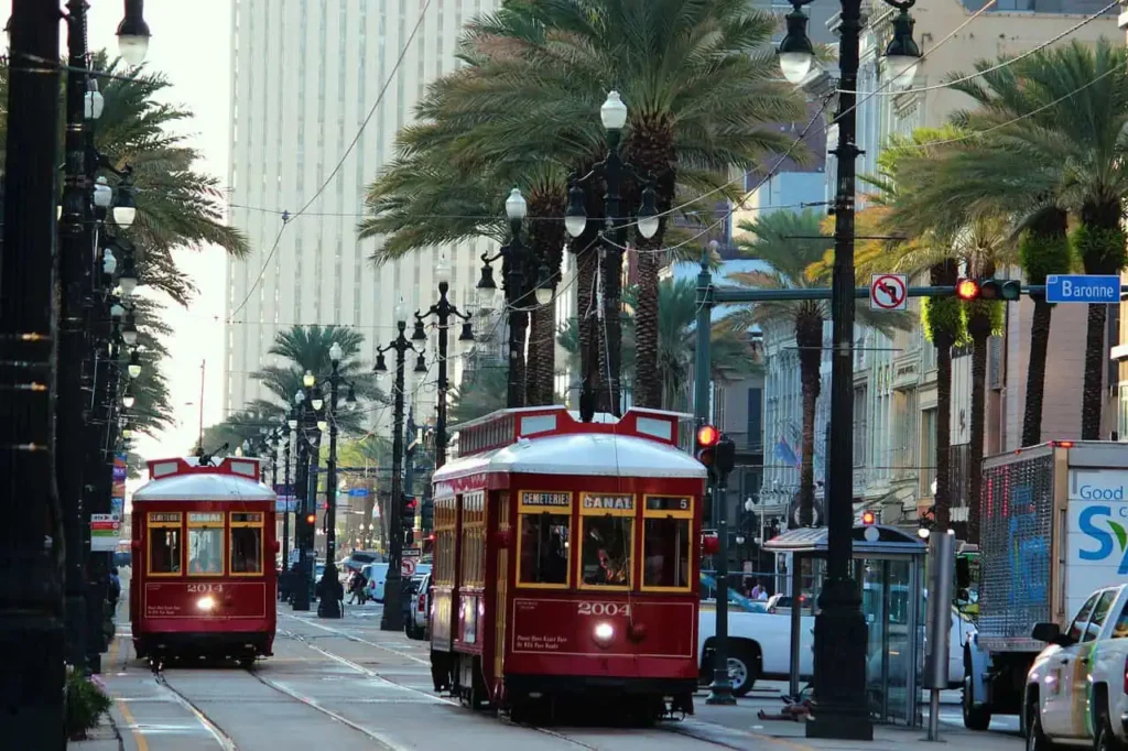 Iconic red streetcars traveling along Canal Street in New Orleans, Louisiana, surrounded by palm trees, historic buildings, and a vibrant cityscape.