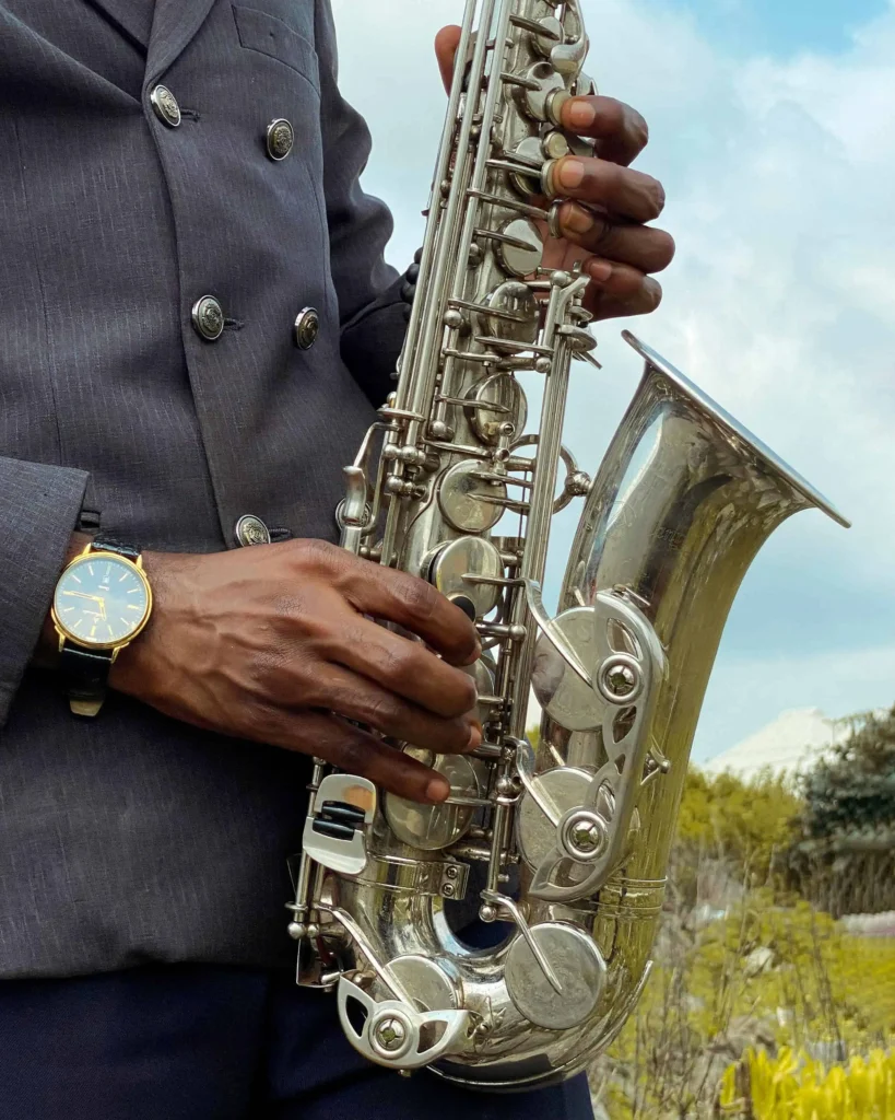 Close-up view of a jazz musician's hands playing a shiny saxophone, showcasing the intricate details of the instrument and a classic wristwatch on the artist's wrist.