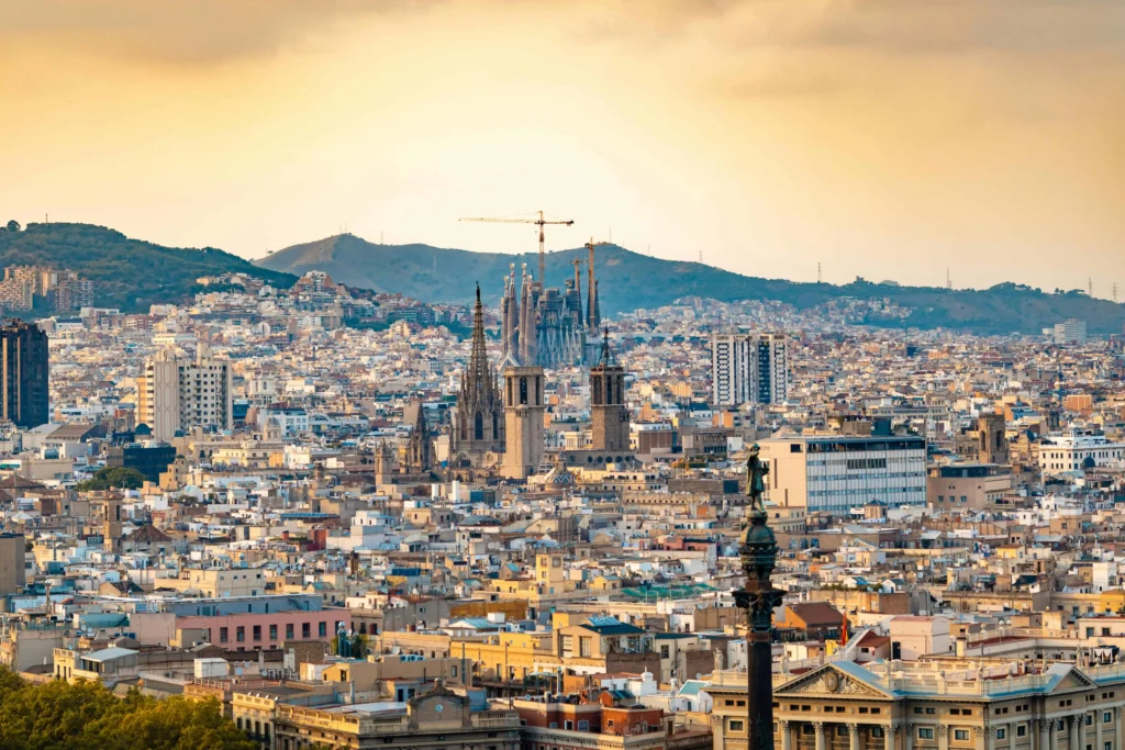 A panoramic view of Barcelona’s skyline with the iconic Sagrada Família towering above the city, framed by a warm sunset glow.