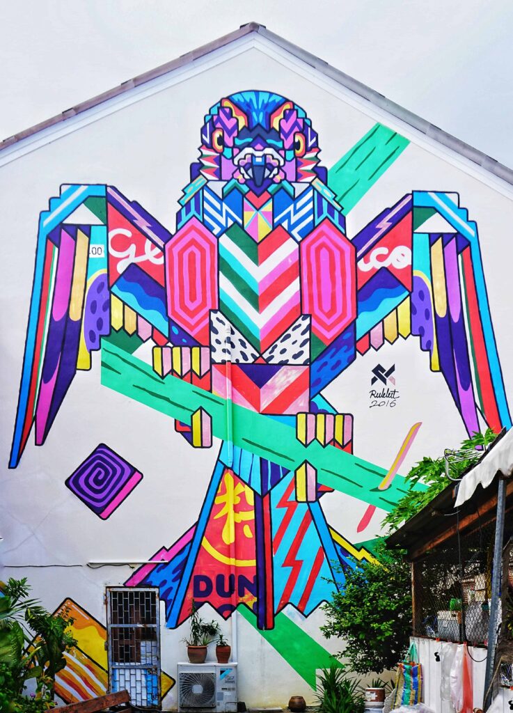 Vibrant and colorful graffiti mural of a stylized bird on a building wall in Thailand, featuring geometric patterns and bold, eye-catching designs.