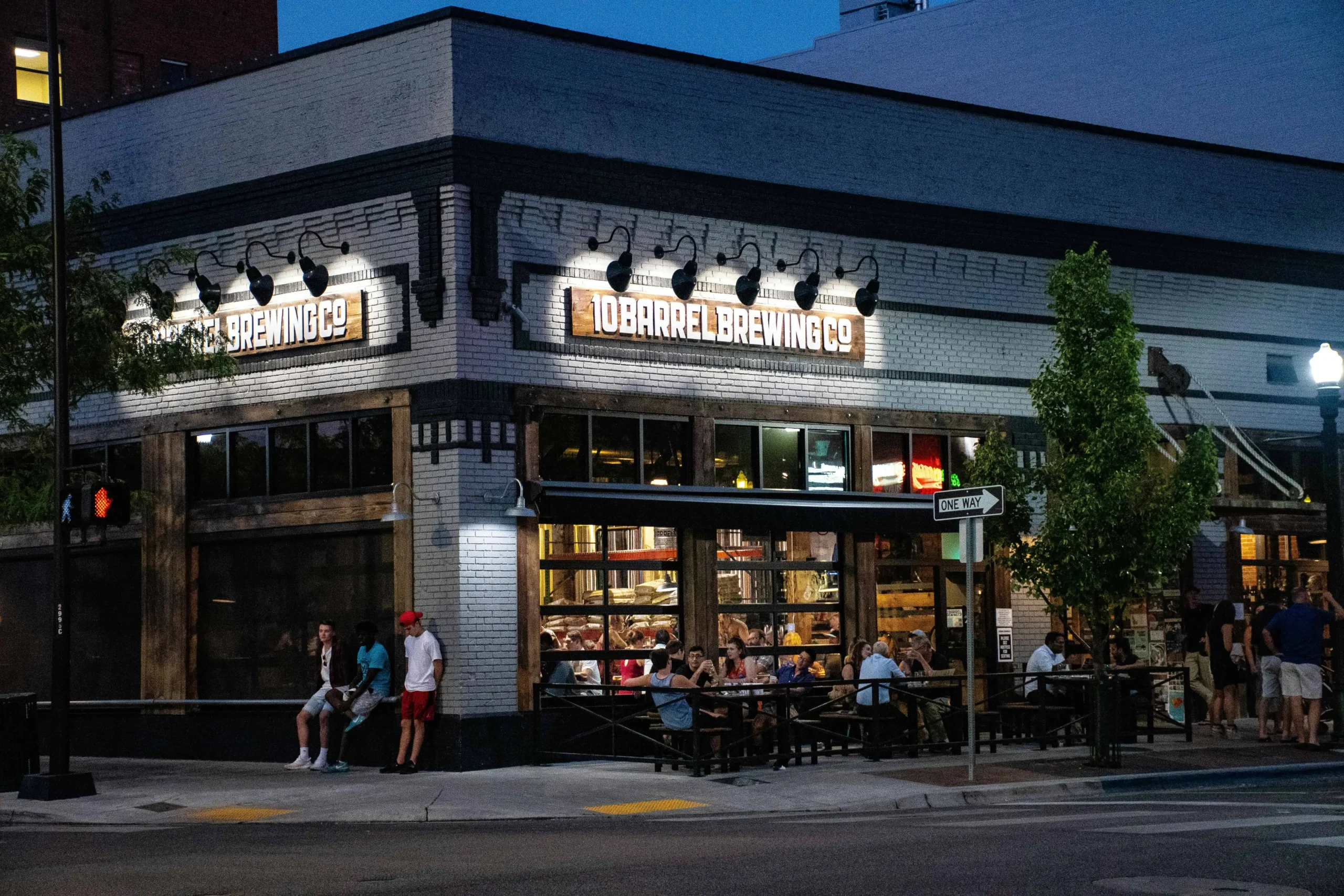 A vibrant brewery with the sign '10 Barrel Brewing Co,' showing people enjoying outdoor seating on a lively street corner in Bend, Oregon, at night