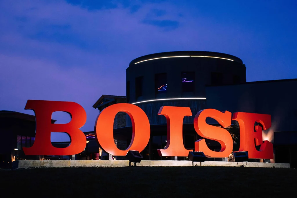 Bold red 'Boise' sign illuminated at night, set against a deep blue evening sky and the modern architecture of downtown Boise