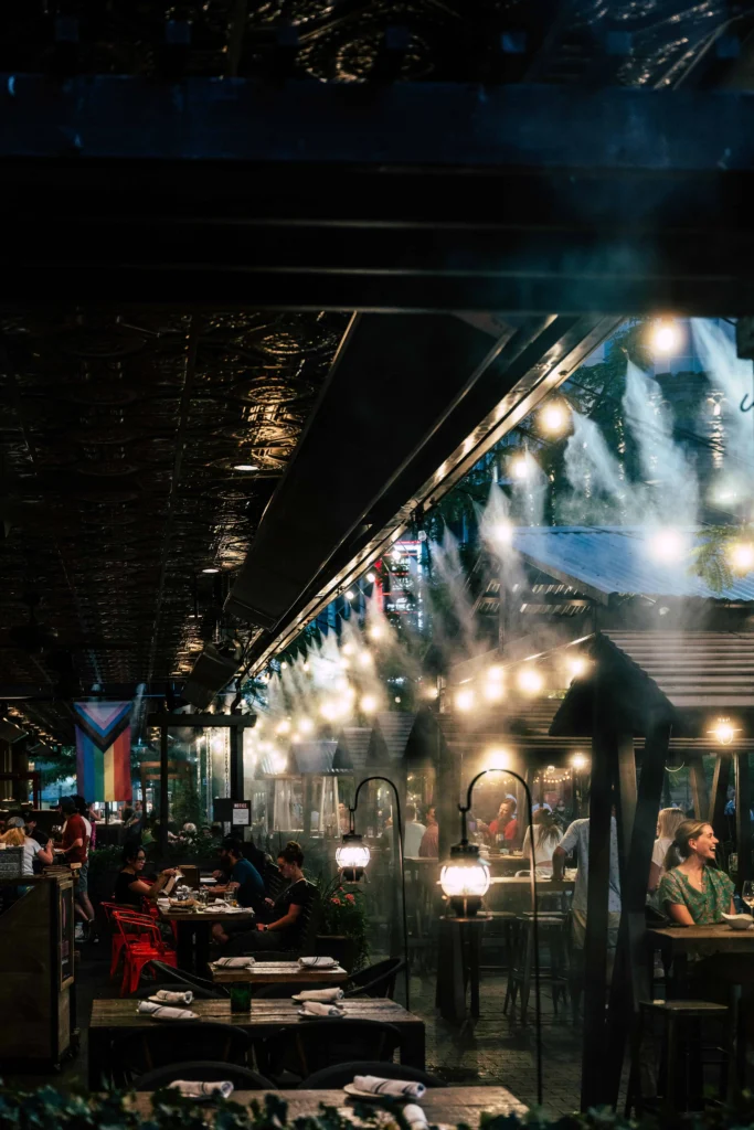 A charming outdoor dining area in Boise, Idaho, lit with ambient string lights, misting fans, and lively evening diners.