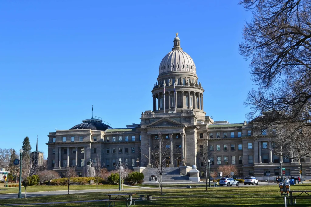 Front view of the Idaho State Capitol building in Boise, Idaho, surrounded by a clear blue sky and lush greenery on a sunny day