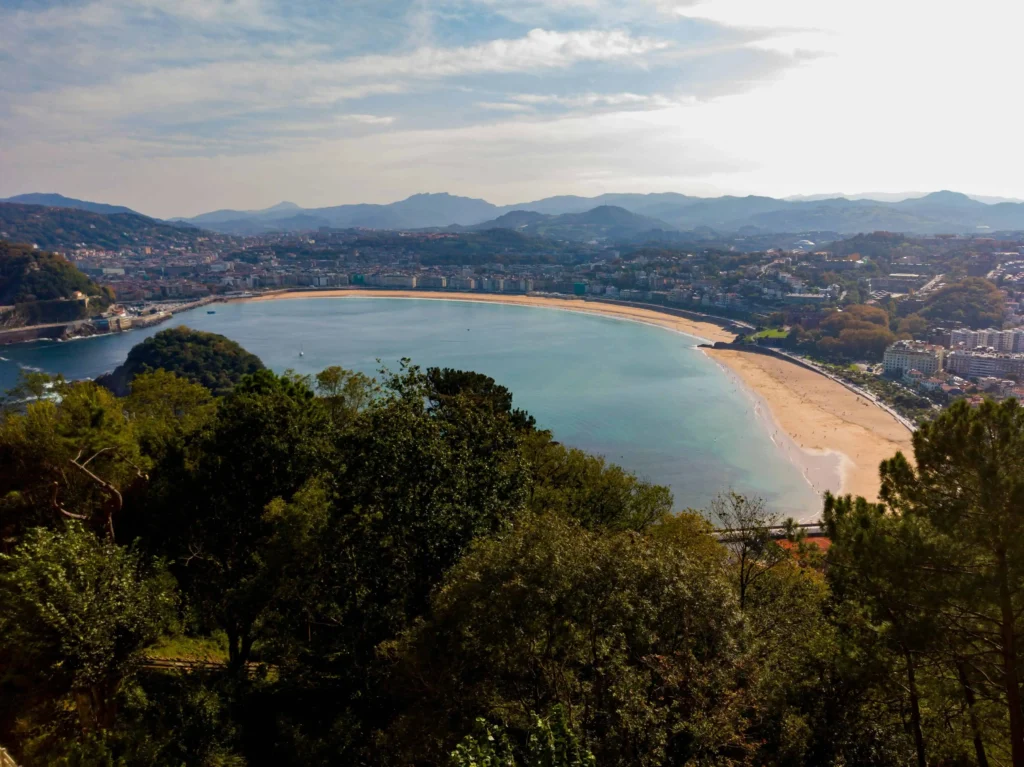 A stunning aerial view of La Concha Beach in San Sebastián, showcasing its golden sands, turquoise waters, and the surrounding cityscape under a clear sky.