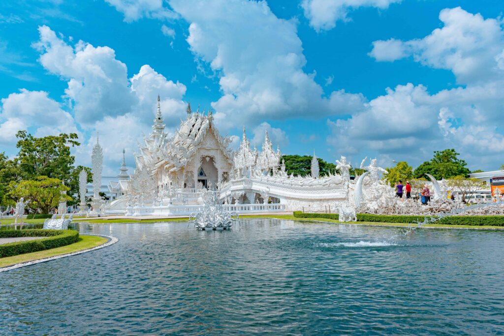 Wat Rong Khun - White Temple in Thailand, showcasing its intricate and pristine white architecture reflected on a serene pond under a vibrant blue sky