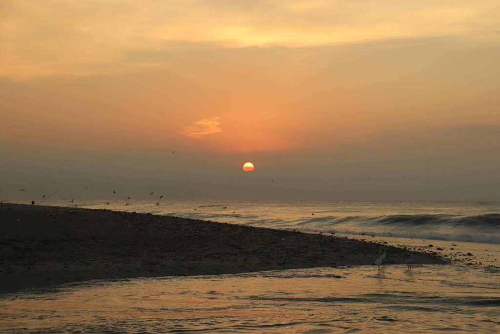 A peaceful beach scene at sunrise, with the sun rising over the horizon and gentle waves washing ashore.