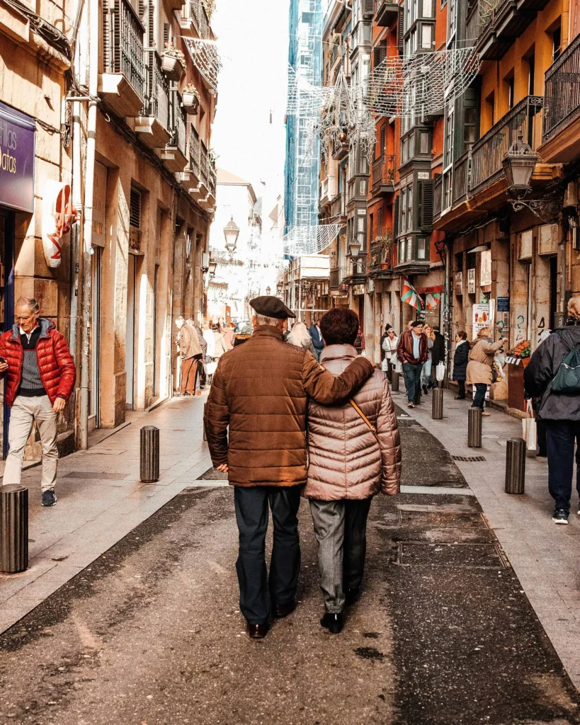 A couple enjoying a stroll through a vibrant historic street in Spain, surrounded by colorful buildings and a lively atmosphere.