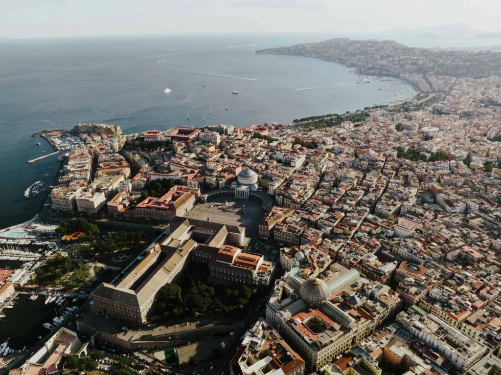 Aerial perspective of Naples, showcasing historic buildings, the Royal Palace, and the Bay of Naples.