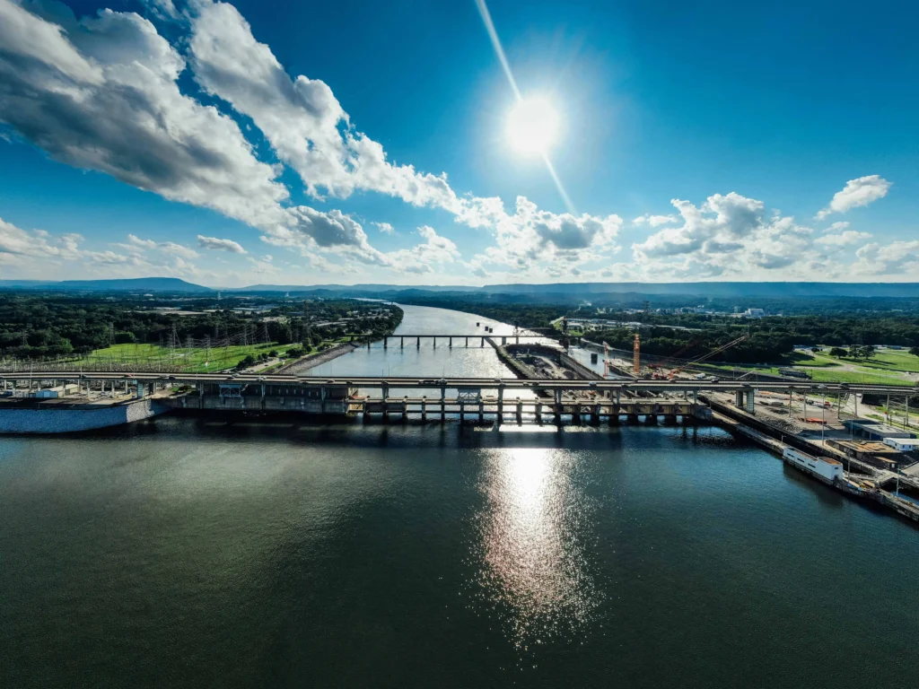 Chattanooga river view under a clear blue sky, showcasing a bridge, shimmering water, and lush green surroundings in the distance