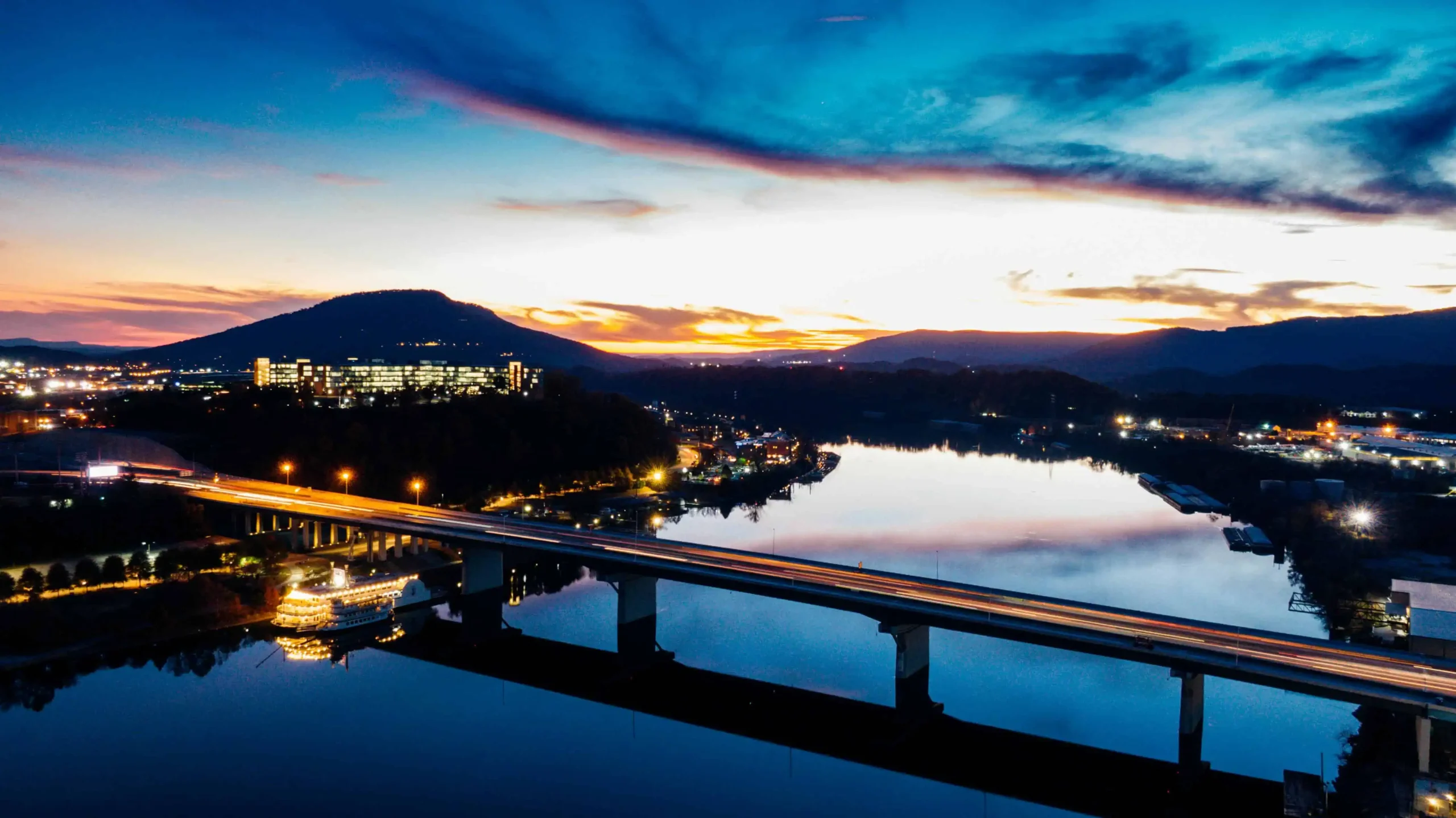 Things to do in Chattanooga: A stunning view of Chattanooga's downtown skyline at sunset, featuring the Tennessee River, illuminated bridges, and Lookout Mountain in the background