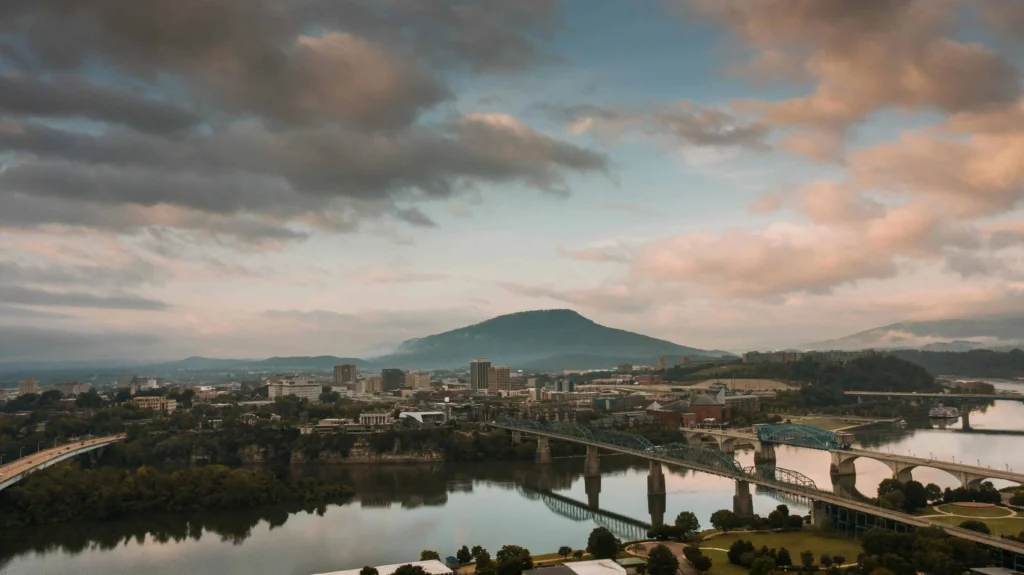 Things to do in Chattanooga: A picturesque view of Chattanooga's downtown skyline, featuring the Tennessee River, iconic bridges, and Lookout Mountain under a cloudy sky.