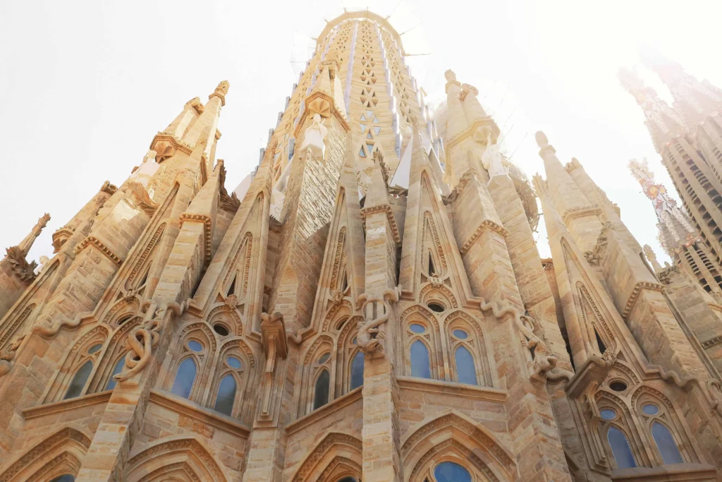 A dramatic low-angle shot of the intricate Gothic facade of Sagrada Família in Barcelona, bathed in bright sunlight