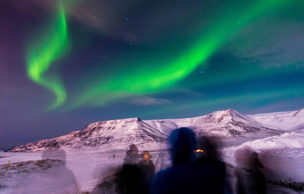 Group of travelers watching the northern lights over snow-covered mountains in Iceland.