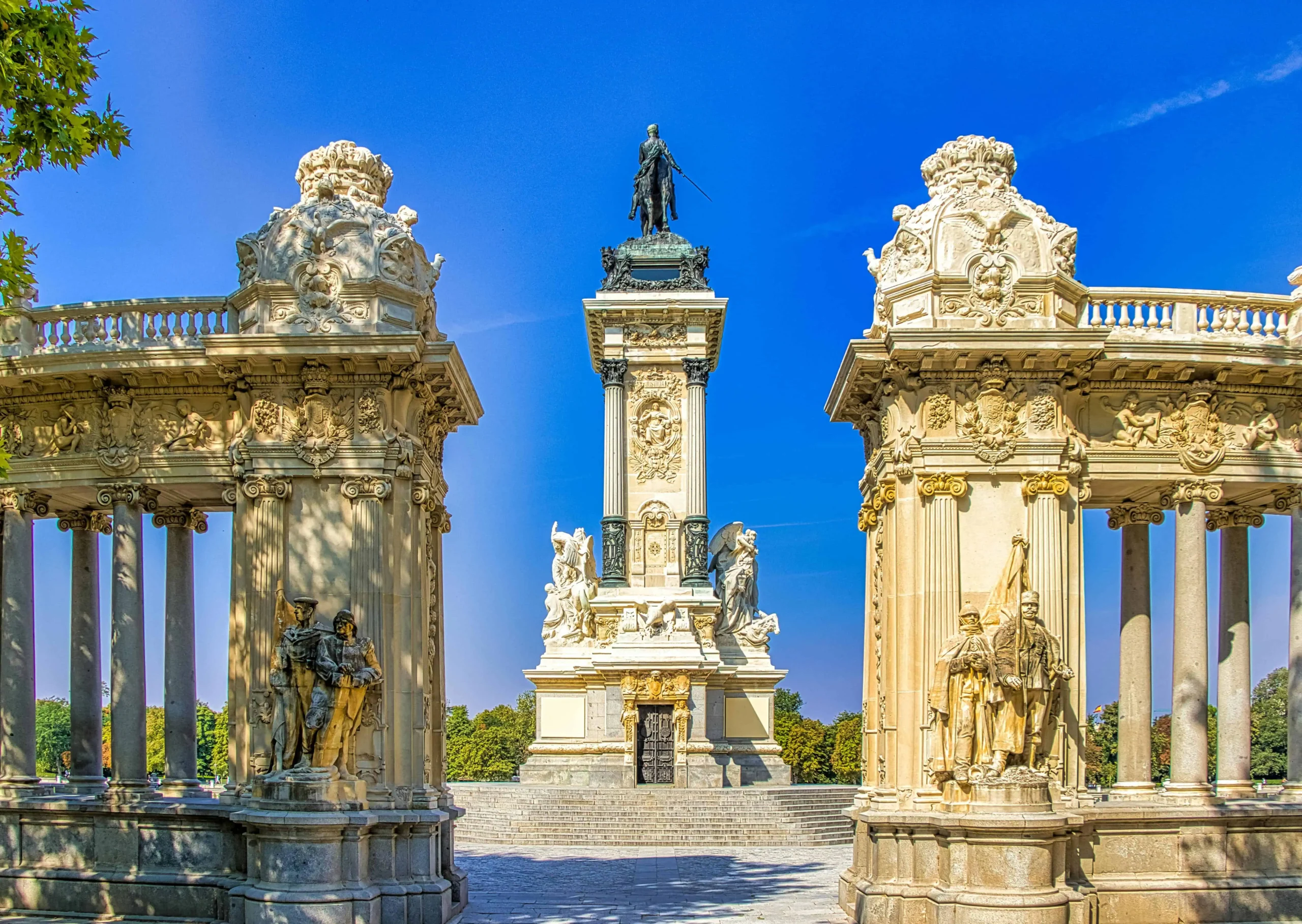 Monument to Alfonso XII in Retiro Park, Madrid, showcasing intricate neoclassical architecture and statues under a vibrant blue sky.