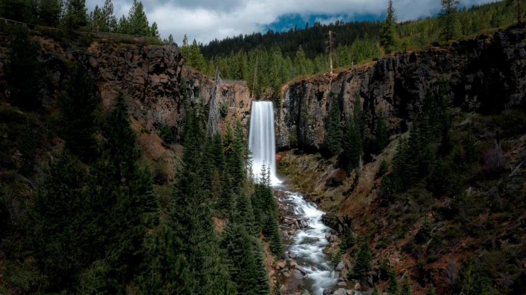 A group of hikers exploring the vibrant moss-covered cliffs near Tumalo Falls in Bend, Oregon, with a powerful waterfall in the background."