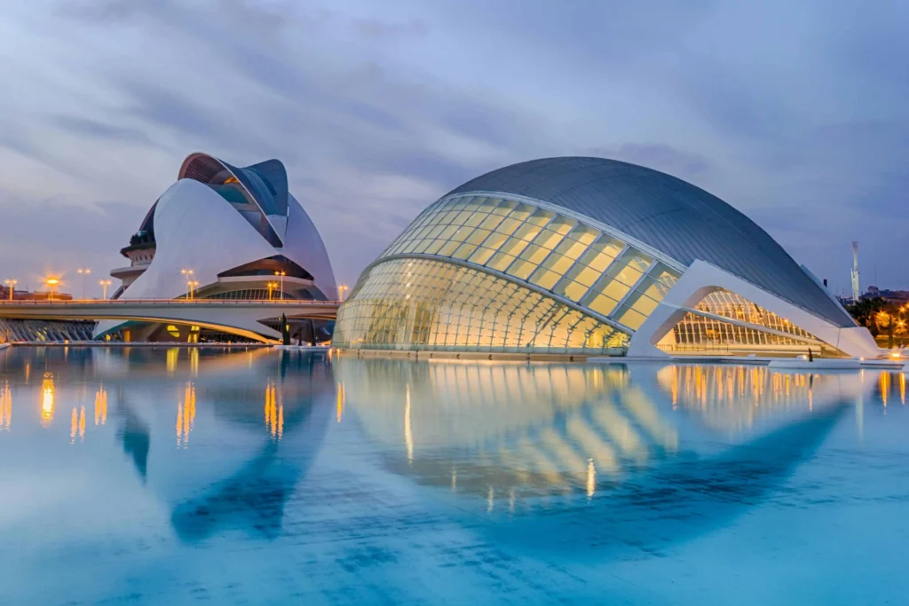 The futuristic architecture of the City of Arts and Sciences in Valencia, Spain, reflected in a serene pool under a twilight sky.