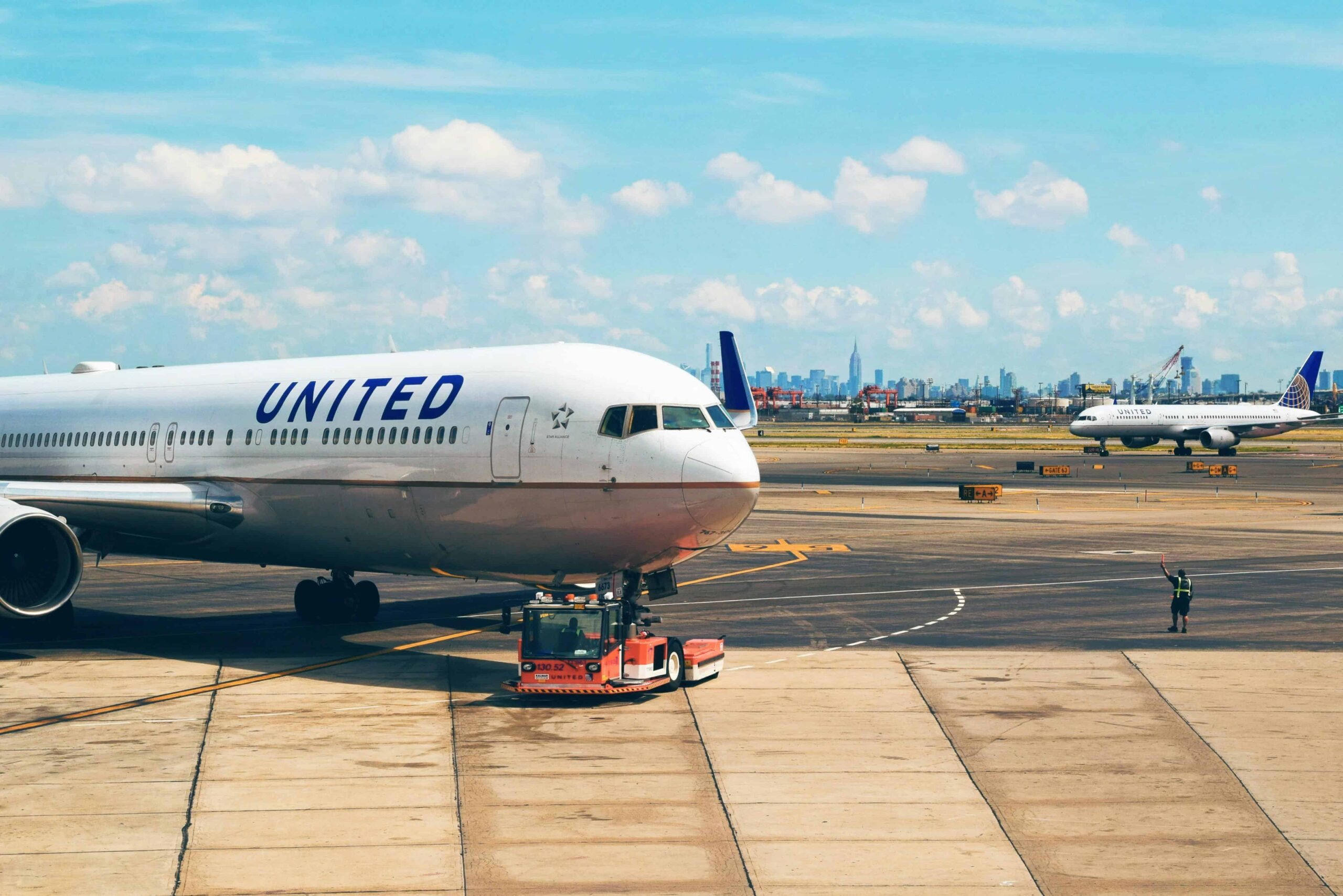 United Airlines plane on the runway at an airport with a city skyline and a clear blue sky in the background.