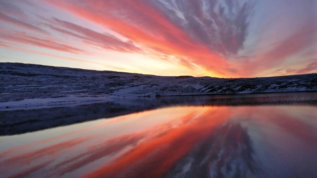 Striking orange and pink hues of a sunset reflecting on a calm lake in Iceland.