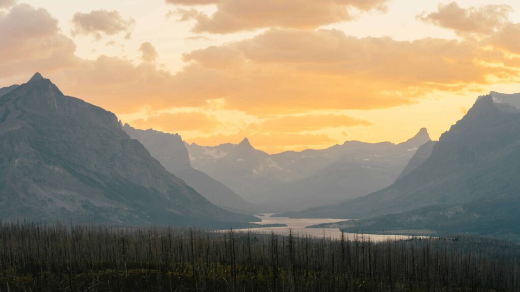 A serene valley view at sunset, with layers of mountain ranges silhouetted against a pastel sky and a winding river flowing through the valley showing the echo bluff state park