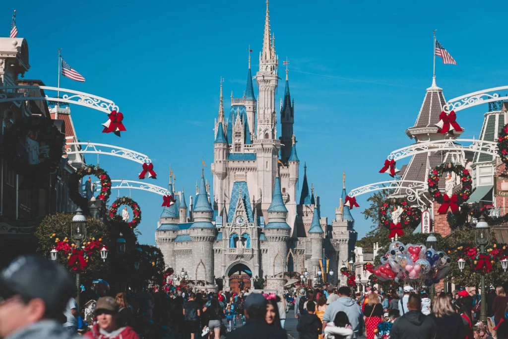 Cinderella Castle at Magic Kingdom in Walt Disney World, Florida, beautifully decorated with holiday wreaths and red bows, surrounded by a lively crowd of visitors under a clear blue sky