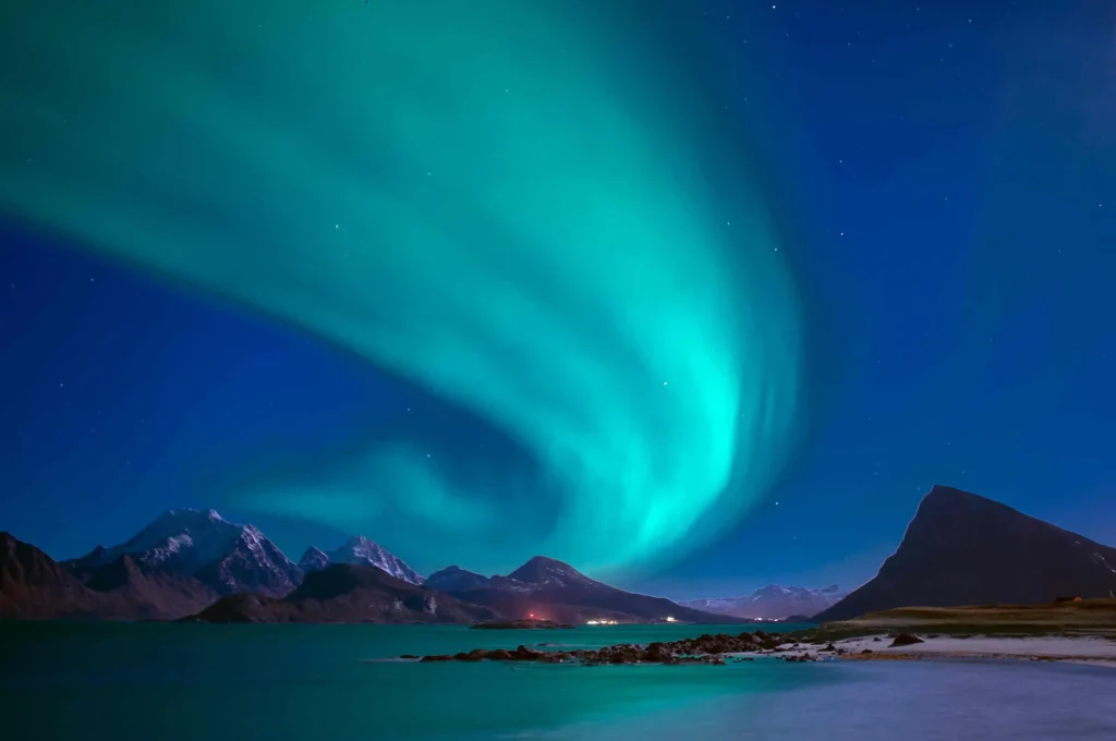 Northern lights dancing over a serene fjord and mountainous landscape.