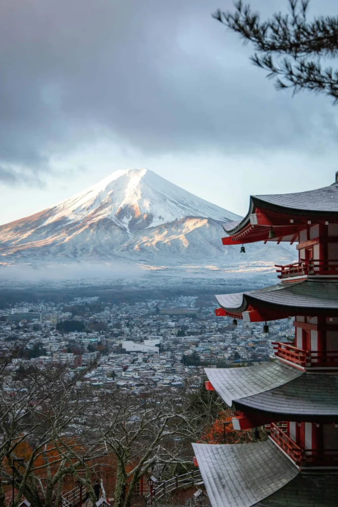 A majestic view of Mount Fuji with snow-covered peaks, seen alongside a red Japanese pagoda during a clear winter day.